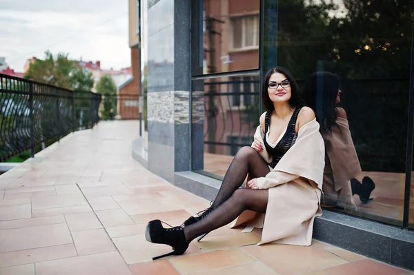 Black hair sexy woman in glasses and coat posed against building — Stock Photo, Image