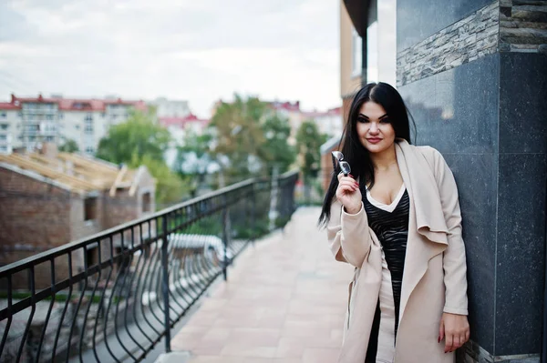 Preto cabelo sexy mulher no óculos e casaco posado contra a construção — Fotografia de Stock