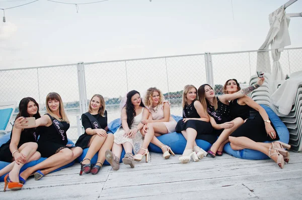 Group of 8 girls wear on black and 2 brides at hen party sitting — Stock Photo, Image