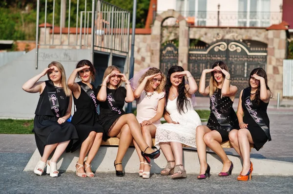 Группа из 7 девушек носят на черном и 2 невесты сидят на скамейке и — стоковое фото