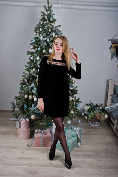 Jolie fille blonde sur robe noire contre le nouvel arbre de l'année avec chris — Photo