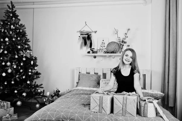 Aranyos szőke lány fekete ruha ajándékokkal ágyon dobozok ag — Stock Fotó