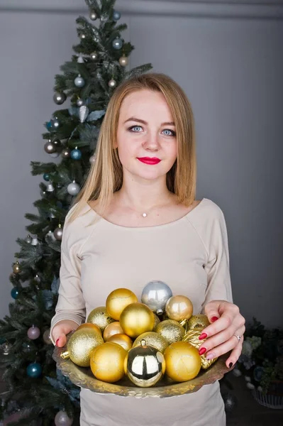Симпатичная блондинка в бежевом платье на фоне новогодней елки с — стоковое фото