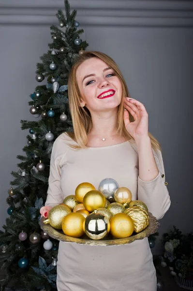 Симпатичная блондинка в бежевом платье на фоне новогодней елки с — стоковое фото