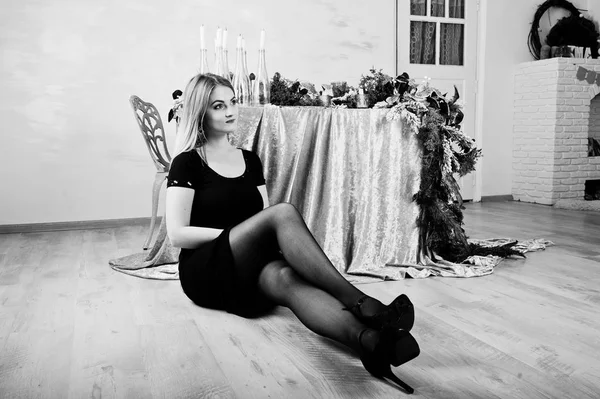 Блондинка в черном платье позировала возле стола с рождественской свечой — стоковое фото