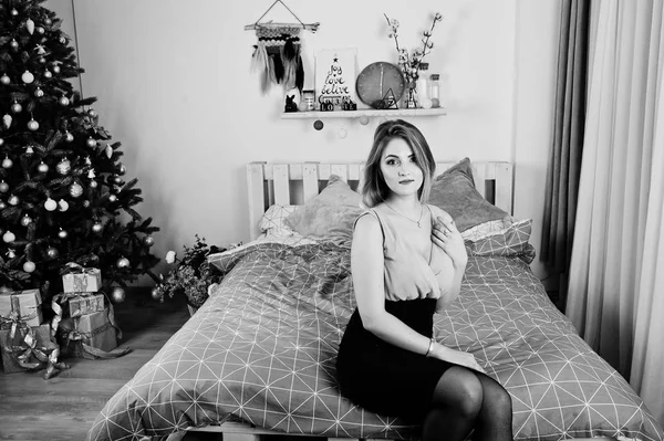 Blonde girl in dress posed on bed near new year tree with christ — Stock Photo, Image