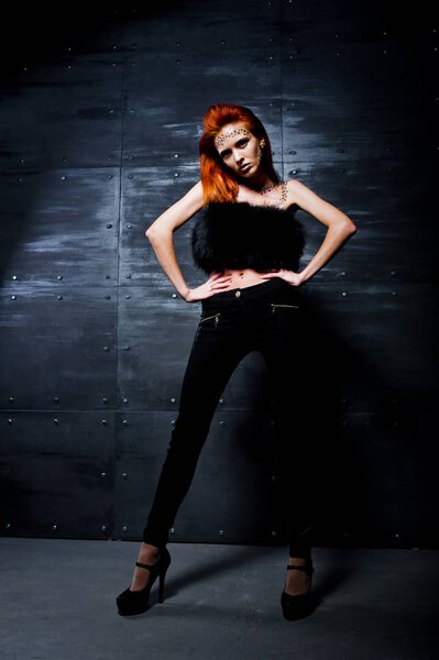 Fashion model red haired girl with originally make up like leopard predator against steel wall. Studio portrait.