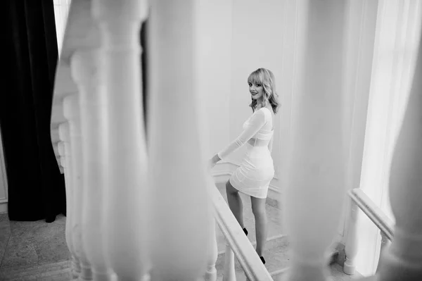 Блондинка в белом платье позировала на белой лестнице коридора . — стоковое фото