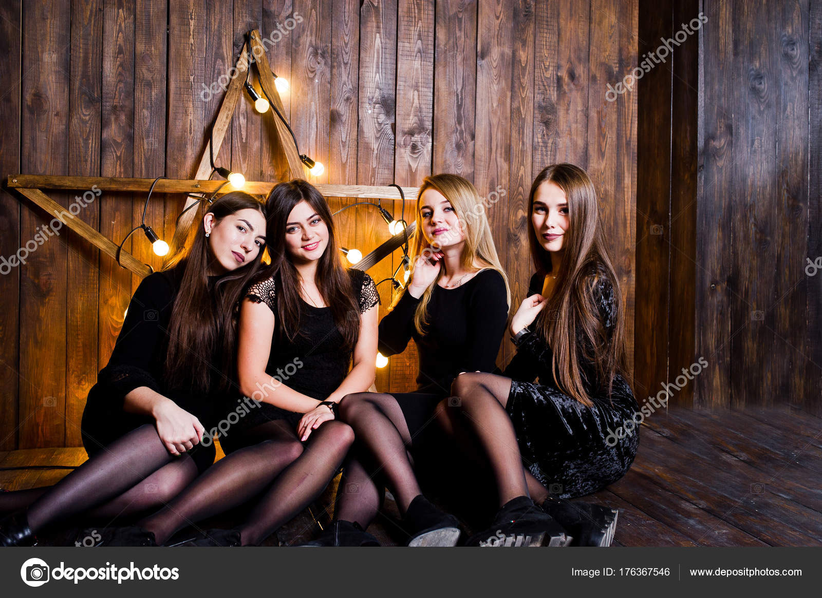 Four cute friends girls wear black dresses against large light c ...