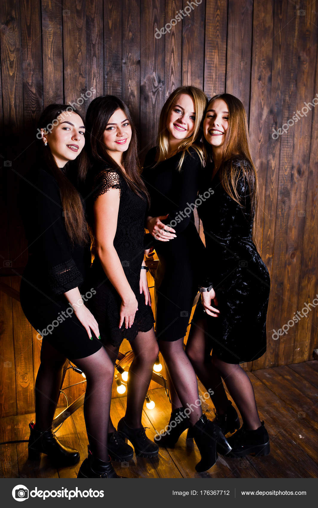 Four cute friends girls wear black dresses against large light c ...