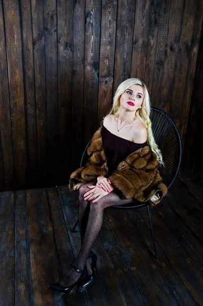 Elegante menina loira desgaste no casaco de pele sentado na cadeira no estúdio — Fotografia de Stock