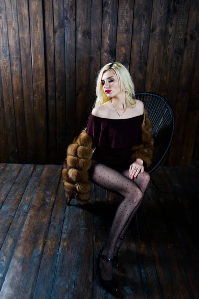 Elegantes blondes Mädchen im Pelzmantel sitzt auf Stuhl im Studio — Stockfoto
