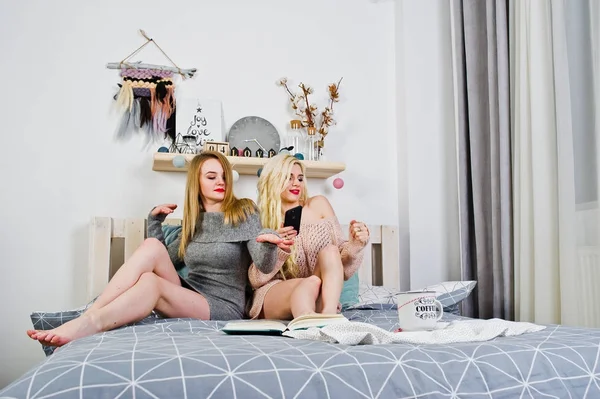 Две элегантные блондинки одеваются в тёплую тунику, сидя на кровати . — стоковое фото