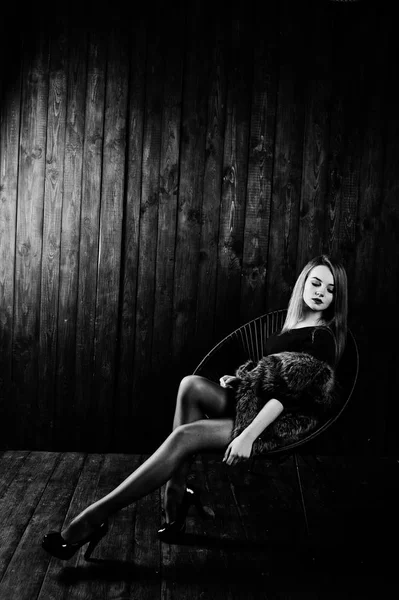 Элегантная блондинка в шубе сидит на стуле в студии — стоковое фото