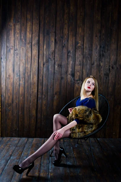 Elegante ragazza bionda indossa una pelliccia seduta sulla sedia in studio — Foto Stock