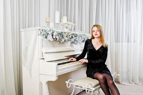 Елегантна блондинка одягнена на чорну сукню проти фортепіано з шиї — стокове фото