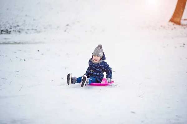 Söt liten flicka med tefat slädar utomhus vinterdag. — Stockfoto