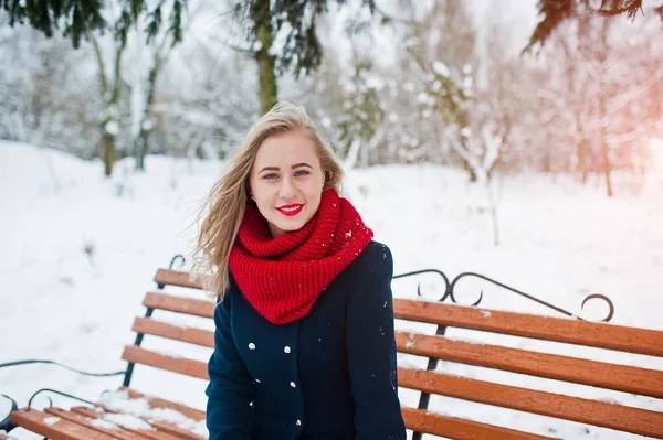 Chica rubia en bufanda roja y abrigo sentado en el banco en el día de invierno —  Fotos de Stock