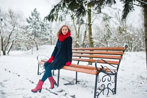 Blond meisje in de rode sjaal en jas zittend op de Bank op de winterdag — Stockfoto