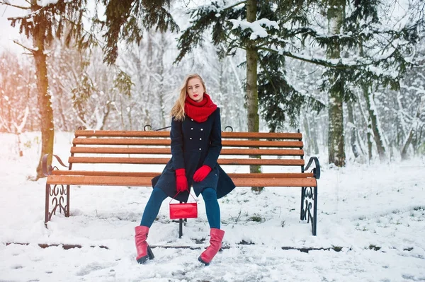 Blond meisje in de rode sjaal en jas zittend op de Bank op de winterdag — Stockfoto