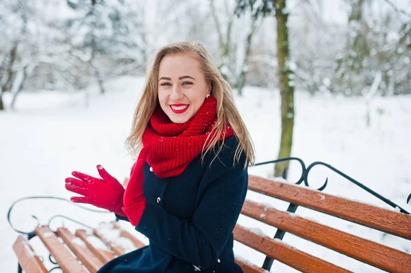 Chica rubia en bufanda roja y abrigo sentado en el banco en el día de invierno —  Fotos de Stock