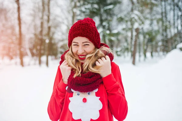 Ragazza bionda in sciarpa rossa, cappello e maglione di Babbo Natale in posa al parco — Foto Stock