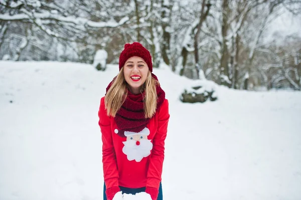 Blondynka w czerwony sweterek szalik, czapkę i santas pozowanie w parku — Zdjęcie stockowe
