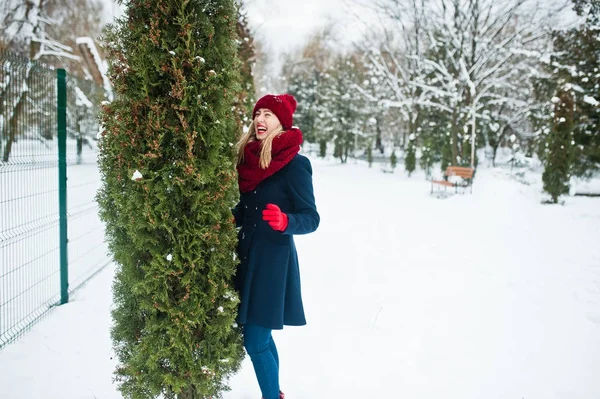 Blond meisje in de rode sjaal en jas lopen in het park op de winterdag. — Stockfoto