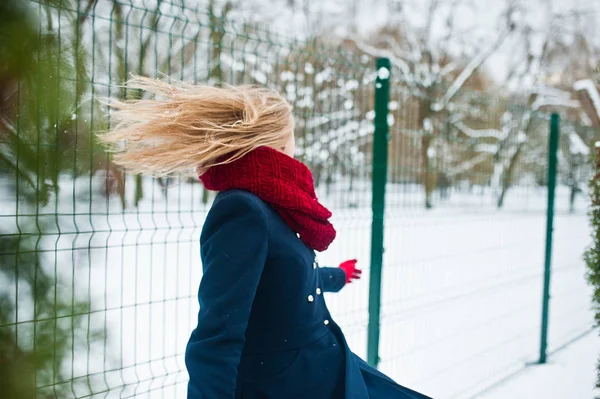 Блондинка в красном шарфе и в пальто прогулка в парке в зимний день . — стоковое фото