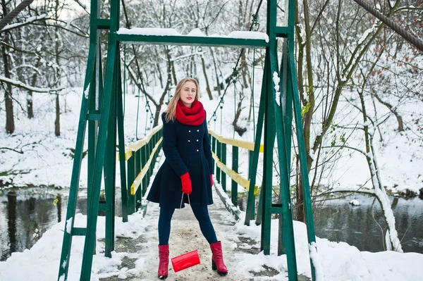 Blond meisje in de rode sjaal en jas lopen op brug in het park op w — Stockfoto