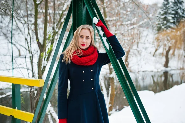 Девушка-блондинка в красном шарфе и пальто прогуливается по мосту в парке — стоковое фото