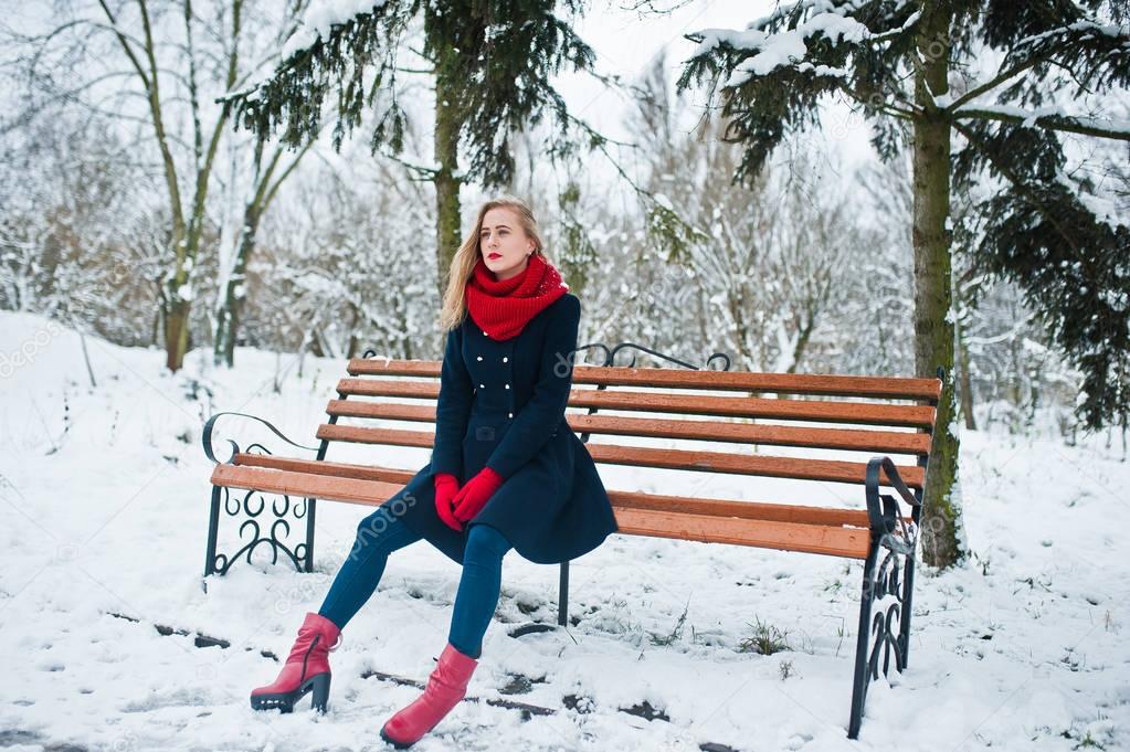Blonde girl in red scarf and coat sitting at bench on winter day