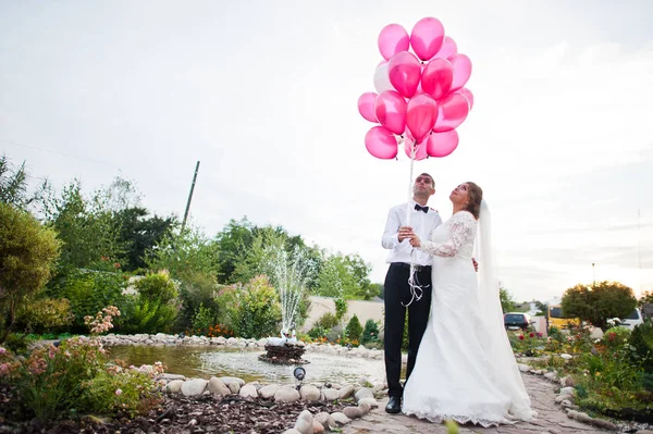 Mooie bruidspaar houden een heleboel roze ballonnen buiten n — Stockfoto