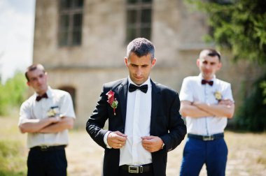 T yanındaki bir güneşli düğün gününde iki sağdıç ile poz damat