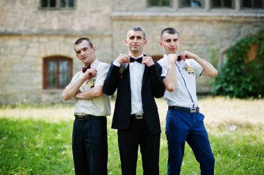 T yanındaki bir güneşli düğün gününde iki sağdıç ile poz damat