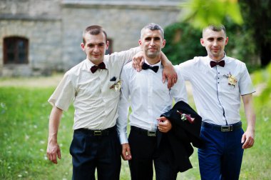 T yanındaki bir güneşli düğün gününde iki sağdıç ile poz damat