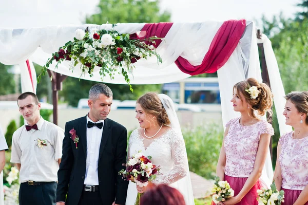 Matrimonio coppia fare voti all'aperto sotto l'arco floreale in fron — Foto Stock