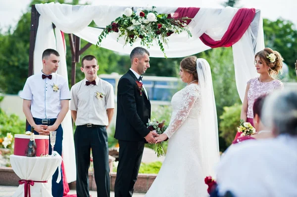 Esküvői pár, hogy fogadalmat a virágos boltív alá szabadtéri sza — Stock Fotó