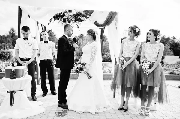 Casamento casal fazendo votos ao ar livre sob o arco floral em fron — Fotografia de Stock