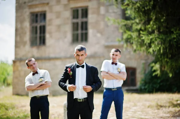 Noivo posando com dois padrinhos em um dia de casamento ensolarado ao lado de t — Fotografia de Stock
