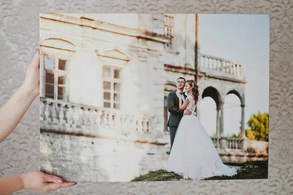 Manos femeninas sosteniendo la foto enorme de la boda en el fondo gris . —  Fotos de Stock