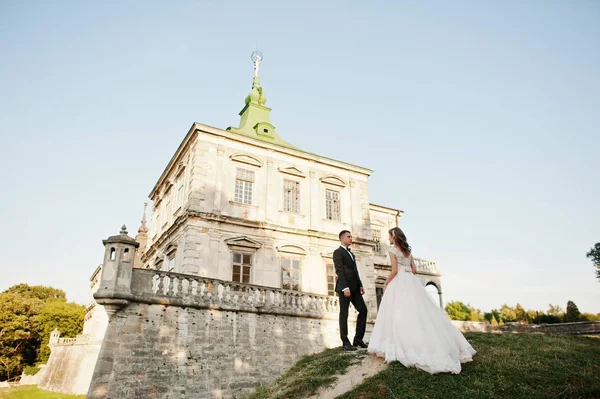 Fabuloso casal de casamentos posando na frente de um velho castelo medieval — Fotografia de Stock