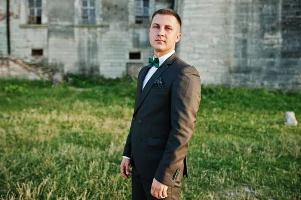 Portrait of a handsome groom standing on the grass next to the c — Stock Photo, Image