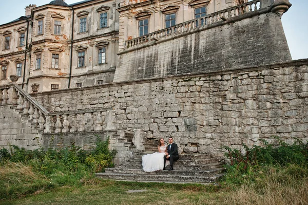 Романтическая свадебная пара, сидящая на лестнице рядом с замком — стоковое фото