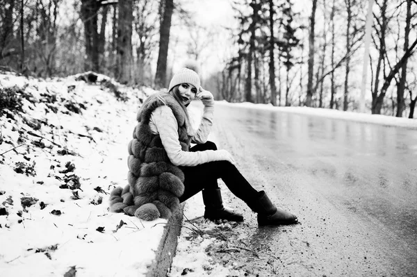 Стильная девушка в шубе и головном уборе в зимний день на сидячем месте — стоковое фото