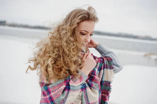 Curly blonde girl in checkered plaid against frozen lake at wint