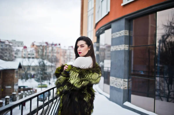 Brunette fille en manteau de fourrure vert à la rue de la ville contre la maison — Photo