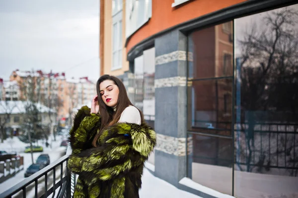 Chica morena en abrigo de piel verde en la calle de la ciudad contra la casa — Foto de Stock