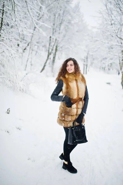 Elégance fille bouclée en manteau de fourrure et sac à main au parc forestier enneigé — Photo