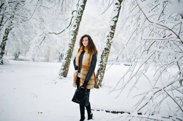 Elégance fille bouclée en manteau de fourrure et sac à main au parc forestier enneigé — Photo